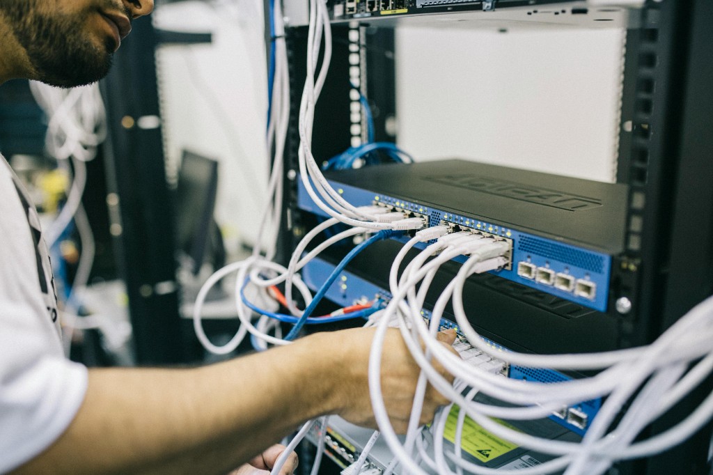 IT technician working in a server rack, connecting network cables to a switch in a data center environment.